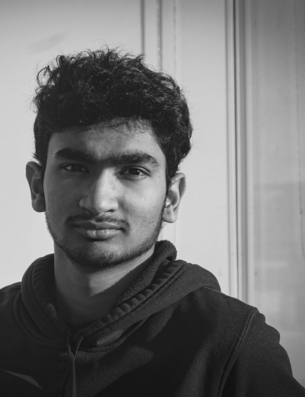 A black and white photo of a boy wearing a hoodie looking straight forward